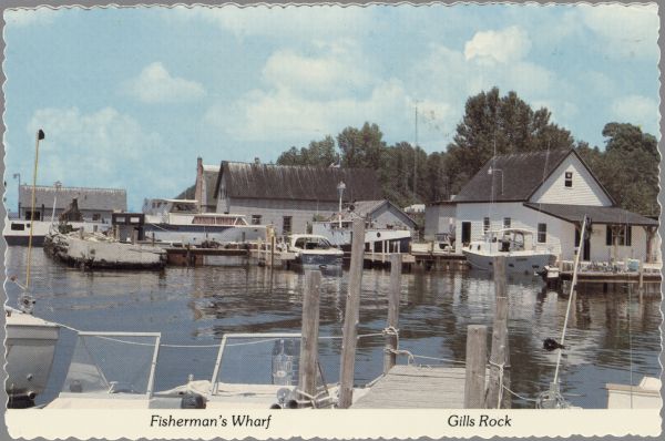 Color view of the marina at Gills Rock. Several privately-owned boats are docked. A wooden pier is in the foreground. Caption reads: "Fisherman's Wharf; Gills Rock, Wis."