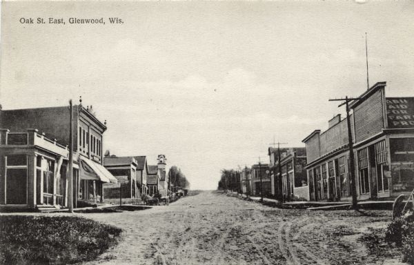 Street scene in a central business district. A church is further down the street on the left. Caption reads: "Oak St., East, Glenwood, Wis."