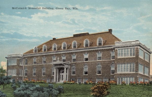 Hand-colored postcard of the McCormick Memorial Building, a nursing home. Columns are at the entrance, and flowers are planted along the ground floor. Rooftop terraces are on each side. Caption reads: "McCormick Memorial Building, Green Bay, Wis."