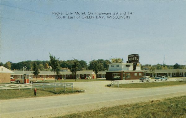 Ektochrome postcard of a roadside motel, with white fencing along the entrance. There is a phone booth at the edge of the parking lot. Caption reads: "Packer City Motel; On Highways 29 and 141, South East of Green Bay, Wisconsin."<p>Text on reverse reads: "Packer City Motel 42 Deluxe Rooms<br>On highways 29 and 141, two miles from downtown<br>Northeast Wisconsin's Largest Ultra-Modern Motel<br>Mr. and Mrs. Leo P. Braspenick<br>Phone: HEmlock 2-8654"</br>