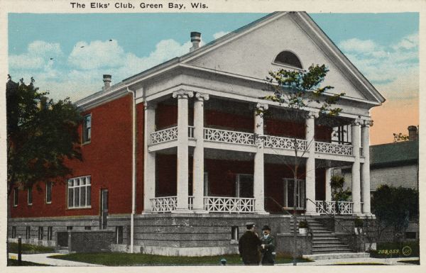 Colorized view of the Elk's Club. The entrance is surrounded by columns. There is a porch and a balcony, and two men are standing on the sidewalk in front. Caption reads: "The Elk's Club, Green Bay, Wis."
