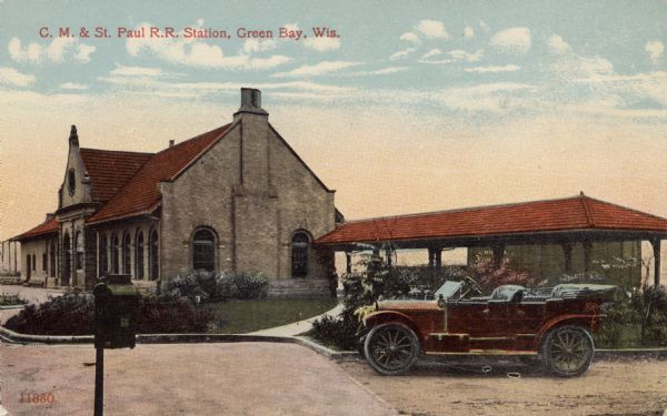 Colorized view of the front and side of the railroad depot. On the right is an automobile parked at the curb. A mailbox is in the foreground on the left. Caption reads: "C.M. and St. Paul R.R. Station, Green Bay, Wis."