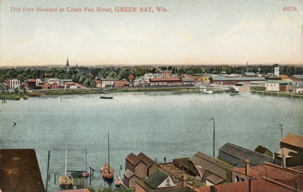Hand-colored postcard elevated view of buildings along the Fox River. Boats moored in the foreground. A train is passing by across the river. Old Fort Howard was a paper mill. Caption reads: "Old Fort Howard at Cross Fox River, Green Bay, Wis."