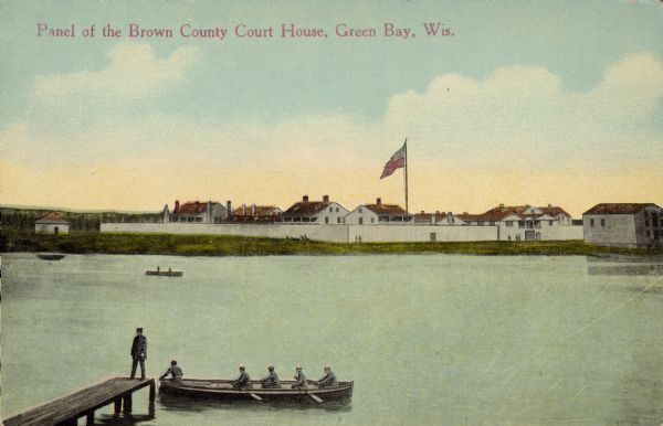 Elevated view across water towards Fort Howard. In the foreground is a man standing on a pier, and in the water nearby are five men rowing in a boat. Caption reads: "Panel of the Brown County Court House, Green Bay, Wis." Text on back reads: "Fort Howard as it appeared in 1850. Built in Green Bay by the U.S. Government in 1816 on Site of French Fort St. Francis, 1718, and later English Fort Edward Augustus, 1761."