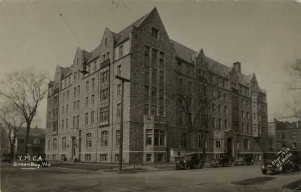 Corner view of the Y.M.C.A., a 5-story stone building. Automobiles parked at the curb.