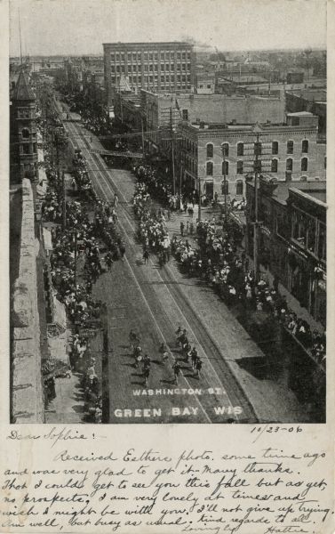 Elevated view of Washington Street during a parade. Crowds are lining the street. Caption reads: "Washington Street, Green Bay, Wis."