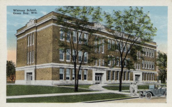 View across street towards the Whitney School. Two people are standing near an automobile parked at the curb. Caption reads: "Whitney School, Green Bay, Wis."