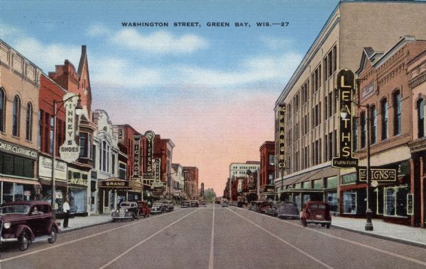 Colorized postcard view of a shopping district lined with shops, and a theater on the left. A Prange's Department Store, and a Leath's furniture store is on the right. Automobiles are parked along the curbs.  Caption reads: "Washington Street, Green Bay, Wis."