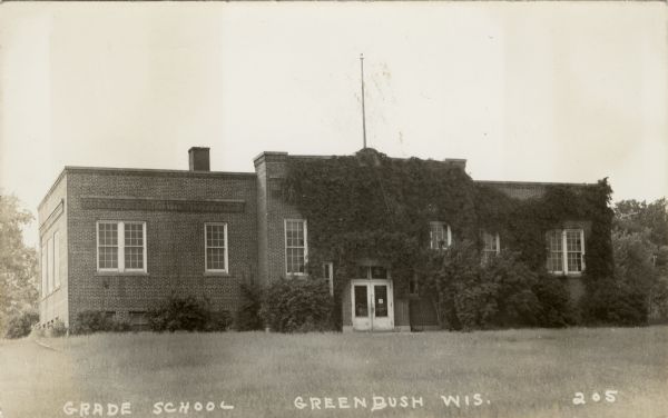 Black and white photographic postcard of an ivy-covered school building. A flagpole is on the roof. Caption reads: "Grade School, Greenbush, Wis."