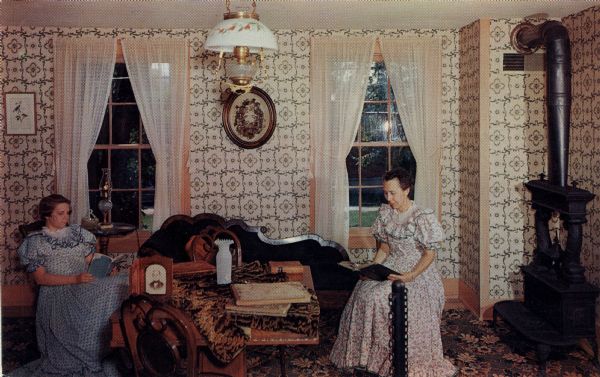 Color postcard of the upstairs parlor, with two women wearing period dress sitting in chairs and reading.

Text on reverse reads: "UPSTAIRS SITTING ROOM, OLD WADE HOUSE, GREENBUSH, WISCONSIN. After Sylvanus Wade opened his inn in 1851, it quickly became known as 'The best on the road.' In this upstairs sitting room, many a guest, especially the womenfolk, whiled away the evening hours. The men were probably in the tap room."
