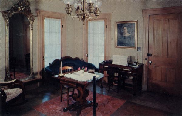 Ektachrome postcard of the Butternut House living room.

Text on reverse reads: "The living room in Butternut House reflects the more luxurious furnishings of a mansion in Greenbush in the early days. The wife of builder Charles Robinson was the eldest daughter of Sylvanus and Betsy Wade."