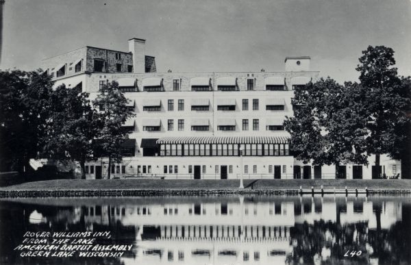 Black and white postcard of a view across water towards the Roger Williams Inn (now the Green Lake Conference Center), main building of the American Baptist Assembly. Caption reads: "Roger Williams Inn, from the Lake, American Baptist Assembly, Green Lake, Wis."