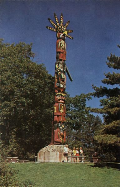 Color postcard of the totem pole at the Indian Village of the American Baptist Assembly. A group of children are standing at the base looking up at it.

Text on reverse reads: "Sala-ku-shid, Totem with Sun on Top, was carved with stone hatchets by Alaskan Indians from a cedar log three feet thick and forty feet long more than two hundred fifty years ago. It is located in the Indian Village."