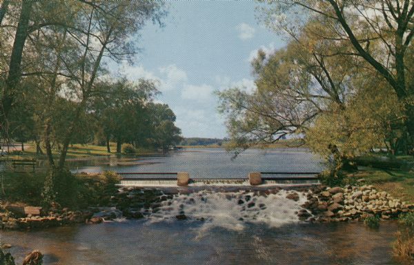 Ektachrome postcard of a dam created waterfall on the Fox River. A city park is on the banks.