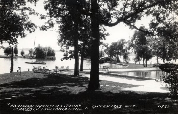 Black and white photographic view of the lakefront and pool at the Northern Baptist Assembly compound. Patio chairs and tables with umbrellas are on the lawn. Caption reads: "'Northern Baptist Assembly formerly Lawsonia Hotel,' Green Lake, Wis."