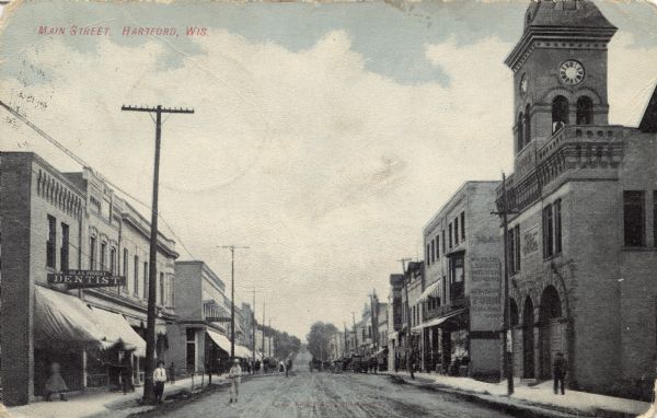 View down Main Street, which is lined with businesses. City Hall is on the right, and a dentist's office is across the street on the left. Caption reads: "Main Street, Hartford, Wis."