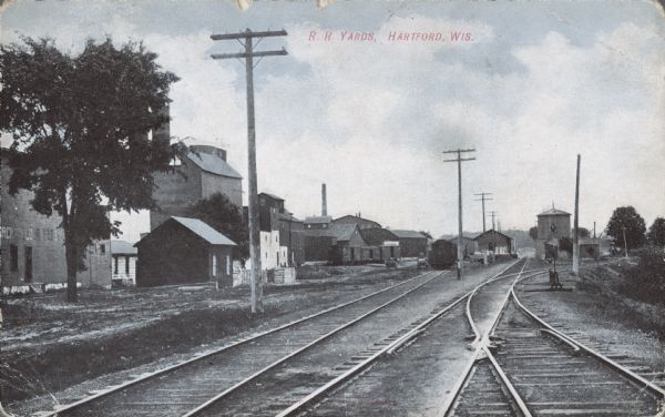 View of the railroad yards. Factories and warehouses are on the left. Caption reads: "R. R. Yards, Hartford, Wis."