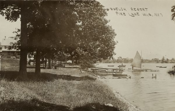 View along shoreline towards the Koelch Resort. There is a sailboat and rowboats in the lake near a pier. Horses are standing under the trees at the shoreline. Caption reads: "Koelch Resort, Pike Lake, Wis."