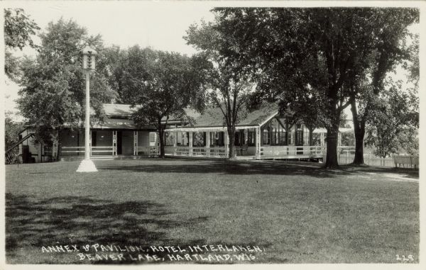 View across lawn towards the annex and pavilion. A large birdhouse is on a tall pole in the lawn in front. Caption reads: "Annex & Pavilion, Hotel Interlocken, Beaver Lake, Hartland, Wis."