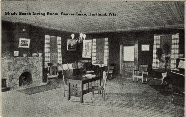 Interior view of a living room (common area) of a resort. A stone fireplace is on the left, and a piano is on the right. Caption reads: "Shady Beach Living Room, Beaver Lake, Hartland, Wis."