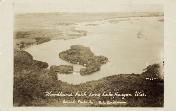 Aerial view of Long Lake and its islands. A road leads out to the biggest island. Caption reads: "Woodland Park, Long Lake, Haugen, Wis. Aerial Photo by N. L. Anderson."