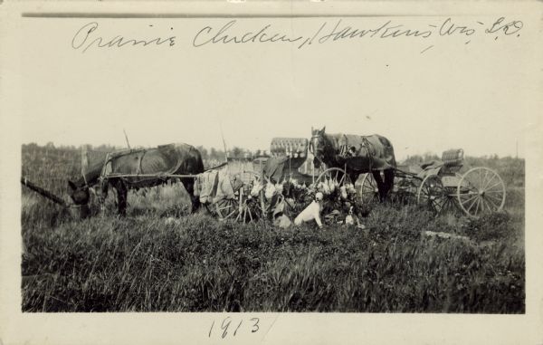 A quarry of dead prairie chickens, hunting dogs, horses and buggies in tall grass. Caption reads: "Prairie Chickens, Hawkins, Wis."