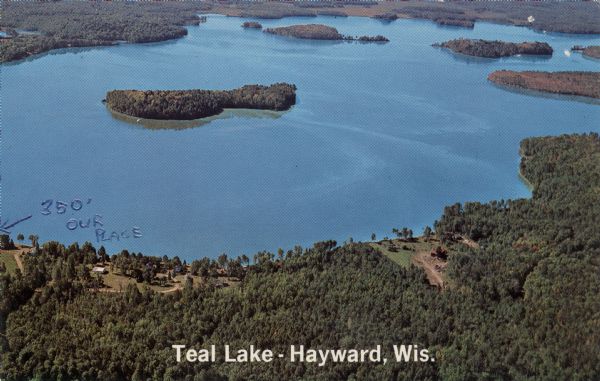 Aerial view of a lake with islands surrounded by forest.

Text on reverse reads: "Joined by a navigable water channel to Lost Land Lake this combined water area is over 2500 acres of good fishing for musky, walleye, bass and pan fish. With its well-timbered shores, good beaches and many islands, Teal Lake is one of Wisconsin's prettiest bodies of water."

Addressed to Governor Knowles.