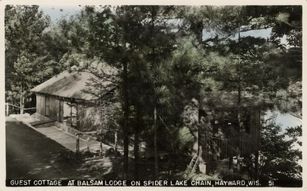 A guest cottage surrounded by pine trees. A lake partially visible in the background.
