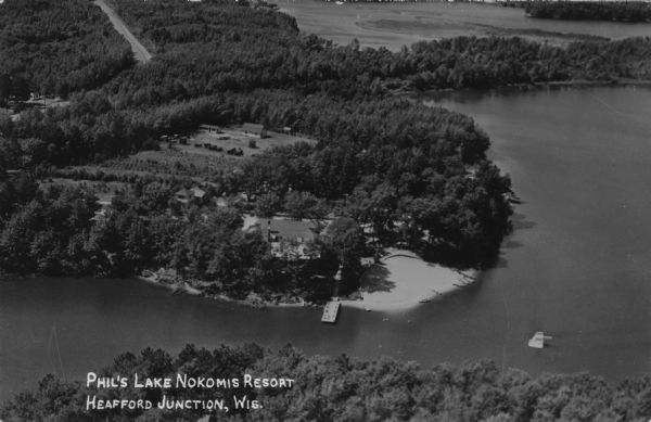 Kodak photographic postcard of an aerial view of a lakeside resort with a large, sandy beach. Caption reads: "Phil's Lake Nokomis Resort, Heafford Junction, Wis."