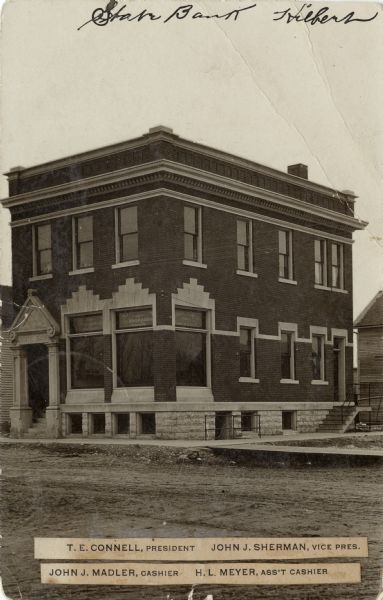 View of the State Bank, a two-story brick building on a street corner. Text on front reads: "T.E. Connell, President; John J. Sherman, Vice Pres.; John J. Madler, Cashier; H.L. Meyer, Ass't Cashier."