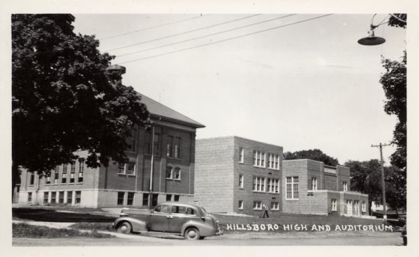 Photographic postcard of the high school. The auditorium and an unknown building is in between them. An automobile is parked next to the sidewalk, and a man is mowing the lawn. Caption reads: "Hillsboro High and Auditorium."