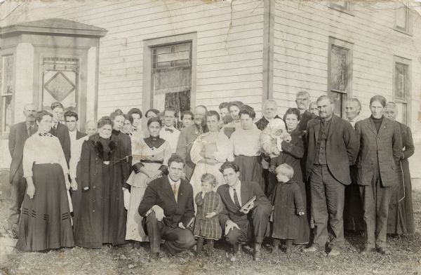 Photographic postcard of a group of men and women, two children and a baby. Two of the women and two of the men are holding hymnals. The correspondence on the reverse refers to a choir.