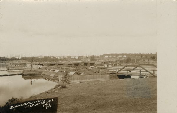 Elevated view of Holcombe, with the dam on the Chippewa River in the foreground. Caption reads: "Birds-Eye View, Holcombe, Wis."