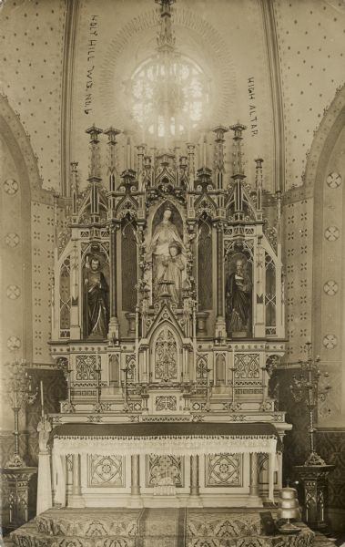 Photographic postcard view of the high altar at Holy Hill. Sculptures of the Madonna and child are in the center, and saints are on either side. There are large candlesticks on bases on either side.