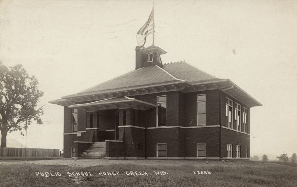 A brick schoolhouse with a bell and flagpole on the roof. Caption reads: "Public School, Honey Creek, Wis."