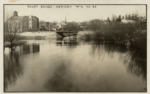 View of the Short Bridge over the Rock River at Horicon. Two men are in a small boat in the river. Caption reads: "Short Bridge, Horicon, Wis."