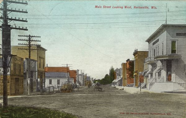 Colorized postcard view down center of Main Street, which is lined with businesses. There are horse-drawn vehicles in the street. Caption reads: "Main Street Looking West, Hortonville, Wis."