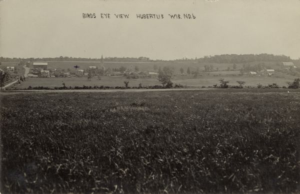 View across fields towards the town of Hubertus. Caption reads: "Birds Eye [sic] View, Hubertus, Wis."