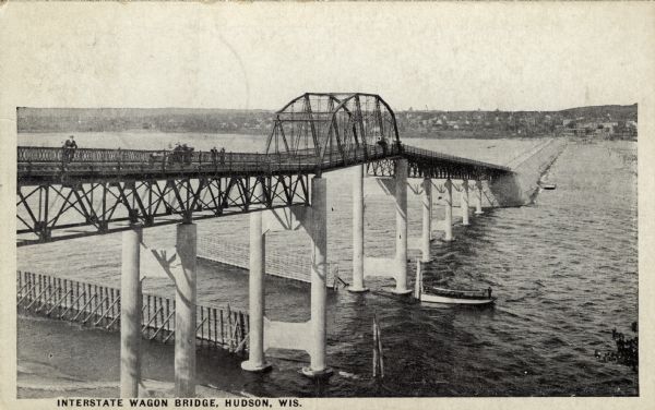 Elevated view of the wagon bridge spanning the St. Croix River. An excursion boat is passing underneath the bridge. Hudson is on the far bank. Caption reads: "Interstate Wagon Bridge, Hudson, Wis."