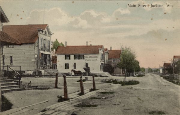 View of Main Street, with storefronts, and the Jackson State Bank. A horse-drawn buggy is parked on the side of the bank. Caption reads: "Main Street, Jackson, Wis."
