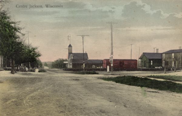 View down road toward the Jackson with the depot on the right. A church is across the railroad tracks. Caption reads: "Centre Jackson, Wisconsin."