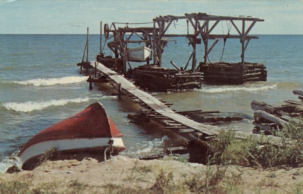 View from shoreline of a fishing dock on Lake Michigan, which has a boat is on a boat lift. Another boat is pulled up on the shoreline.