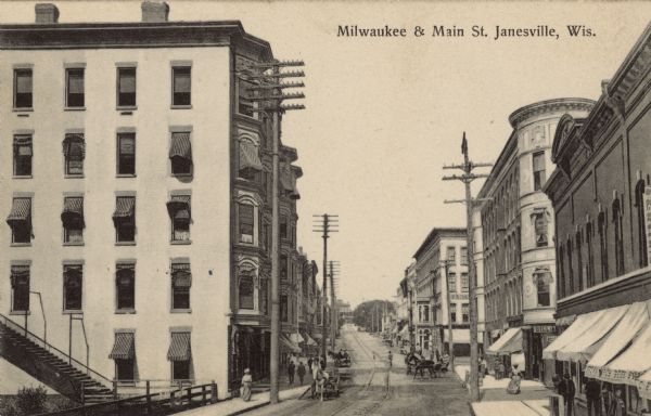 Slightly elevated view of a downtown street, with railroad or streetcar tracks running down the center, and horse-drawn vehicles. Caption reads: "Milwaukee and Main St. Janesville, Wis."