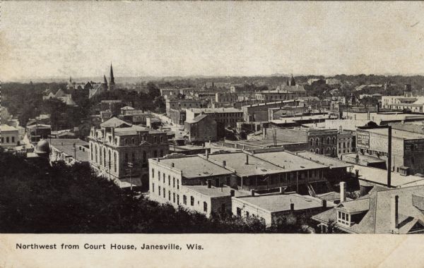 Elevated view of central Janesville from the the courthouse. There are signs advertising Parker Pens and Coca-Cola. Churches are on the horizon. Caption reads: "Northwest from Court House, Janesville, Wis."