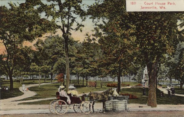 View across street towards a park. There are women sitting in a carriage at the curb. A fountain can be seen among the trees. Caption reads: "Court House Park, Janesville, Wis."