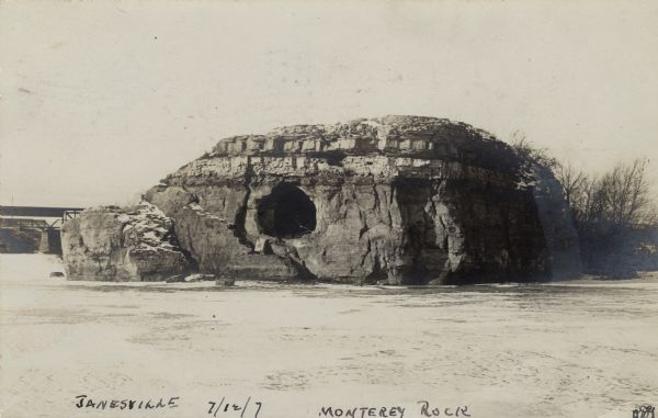 View of Monterey Rock from the Rock River. There is a cave in the center, and a bridge in the distance.