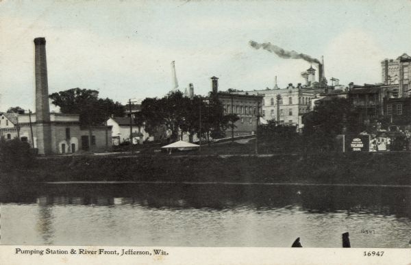 View across water towards the Pumping Station on the riverfront. Central Jefferson is in the background. There are billboards on the right, with one that reads: "Chew Whites Yucatan Gum." Caption reads: "Pumping Station & River Front, Jefferson, Wis."