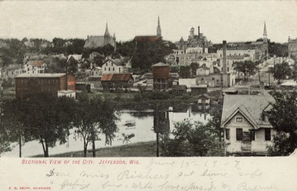 Colorized elevated view of Jefferson with numerous churches, businesses and residential homes, and a body of water in the foreground. Caption reads: "Sectional View of the City, Jefferson, Wis."