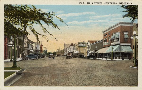 View of Main Street lined with commercial buildings. Automobiles are parked at the curb and street lamps are at the corners. Caption reads: "Main Street, Jefferson, Wisconsin."