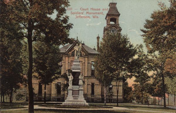 View toward the Soldiers' Monument with three statues on a pedestal, and the Court House behind it. A clock tower is to the right of the entrance behind trees. Caption reads: "Court House and Soldiers' Monument, Jefferson, Wis."